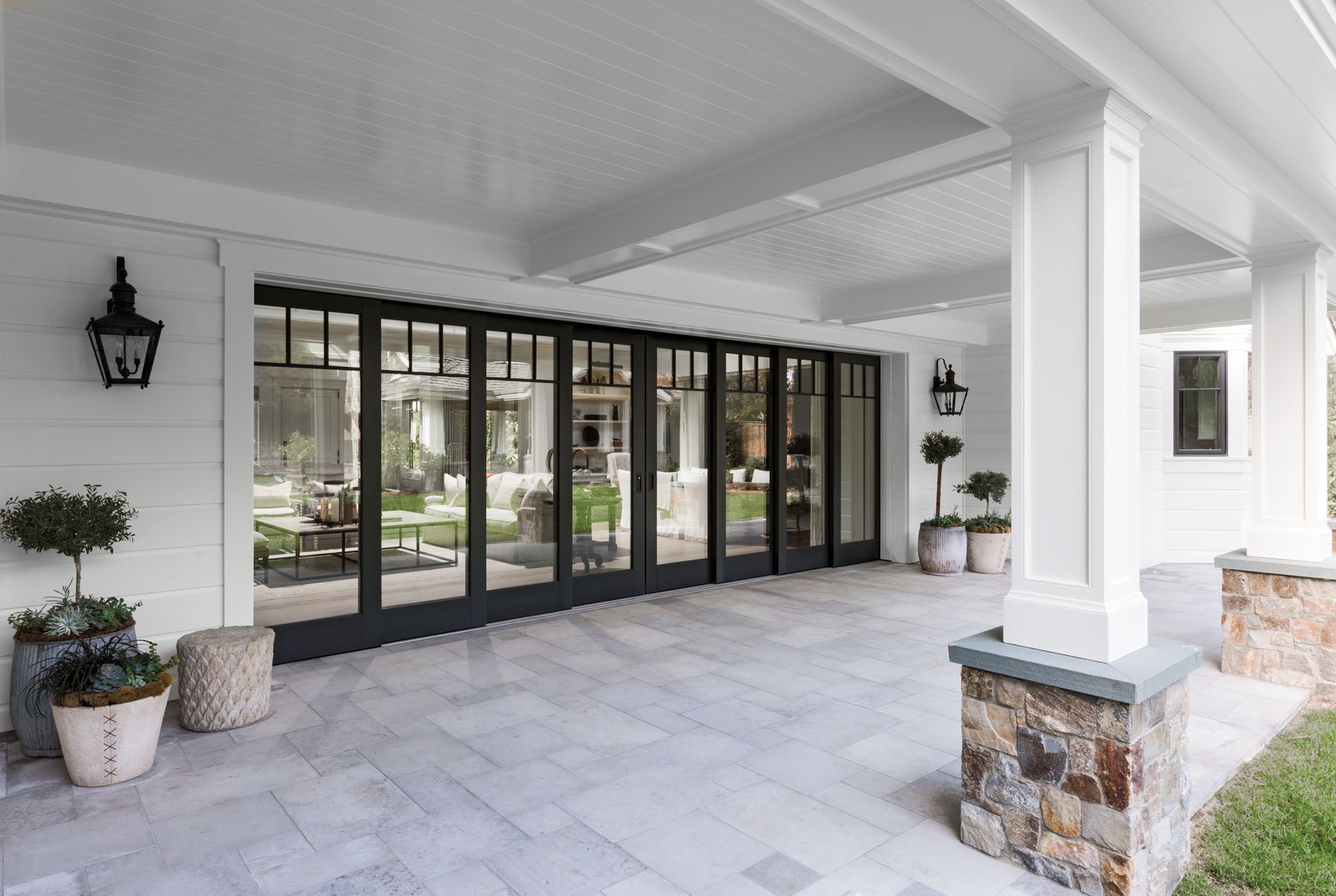 Covered patio with large black framed glass doors, white columns, and gray stone flooring.