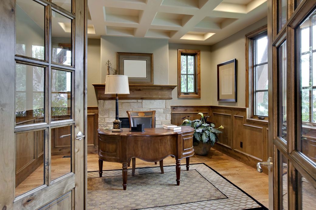 Elegant home office with a wooden desk, fireplace, and windows.