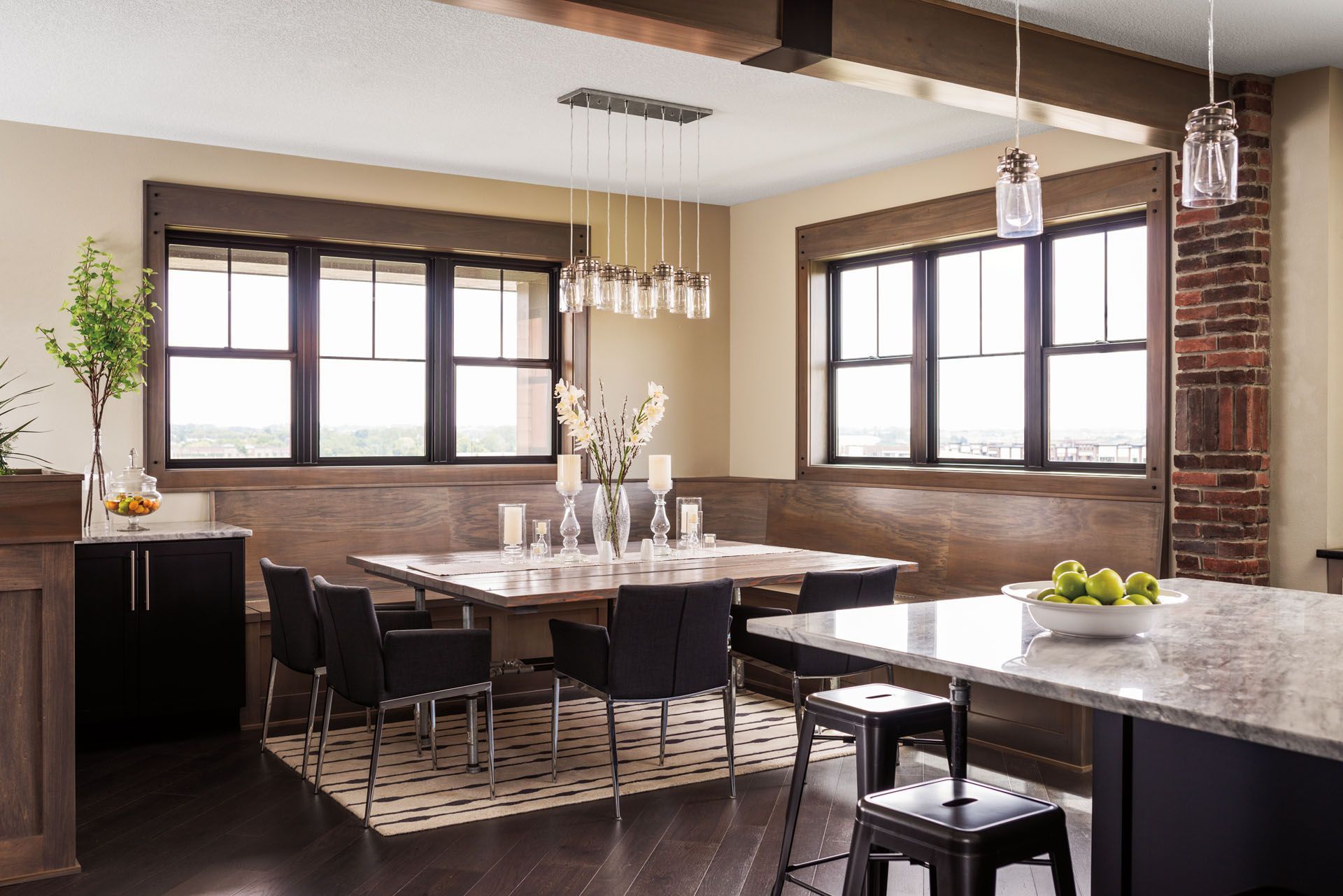 Modern dining area with wooden table, black chairs, windows, and brick column.