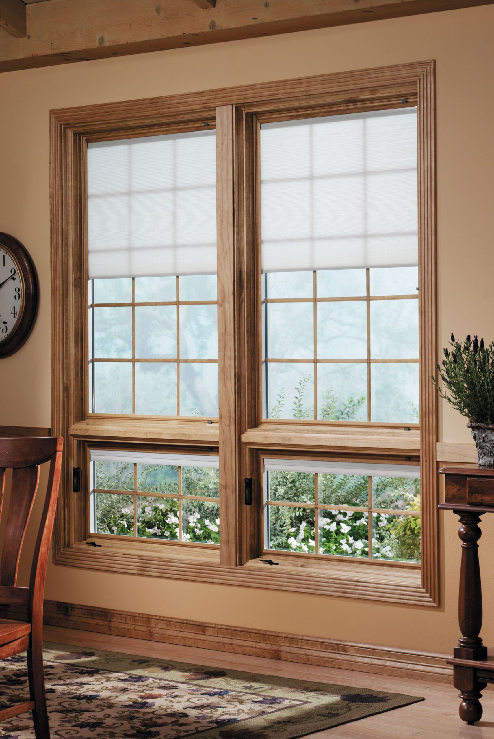 Two wooden-framed windows with white blinds and a view of greenery; set in a room with beige walls and a rug.